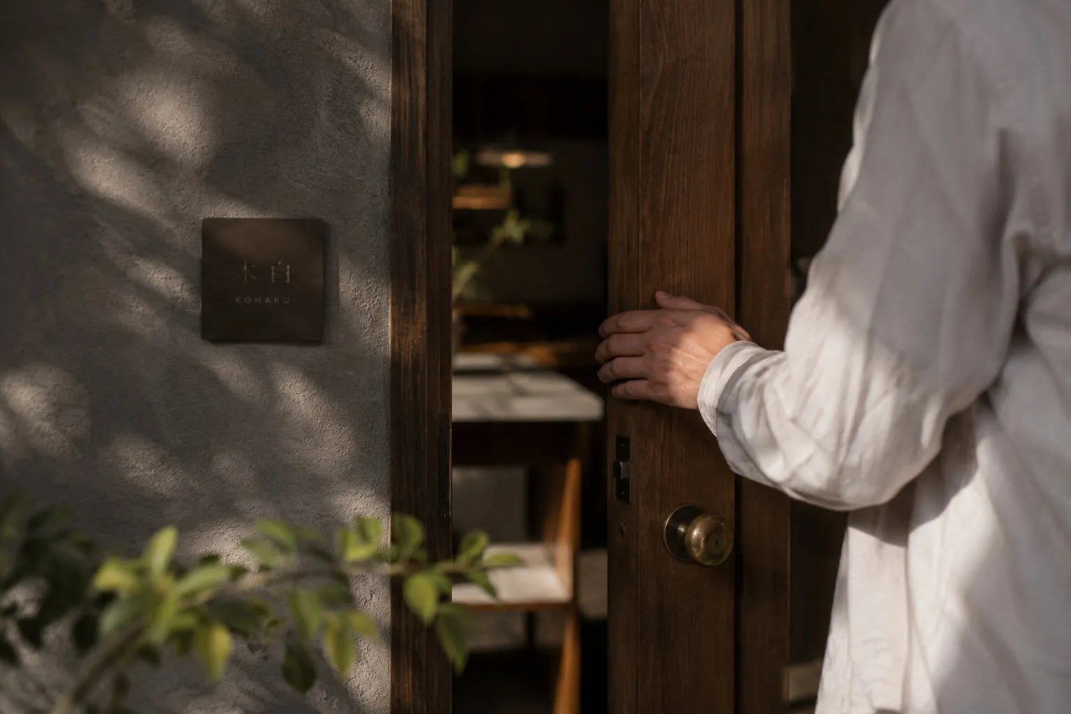 A hand pushes open the door of a venue, engraved plaque at the entrance.